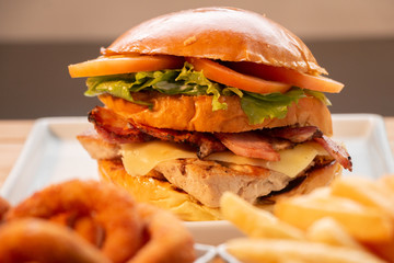Sanduíche de filé de frango com salada de tomate e alface em pão com bacon e queijo em prato branco com porção desfocada antes da apresentação do prato 