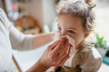 Unrecognizable father blowing nose of small sick daughter indoors at home. - obrazy, fototapety, plakaty