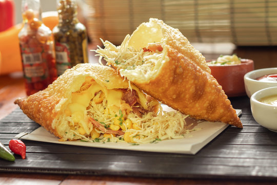 Pastel da culin&aacute;ria brasileira com recheio de frango desfiado com milho e salsa encima de uma esteira preta na mesa de um restaurante  com molho de maionese ketchup mostarda e pimenta    