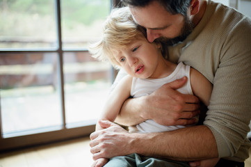 Father with small sick unhappy son indoors at home, comforting him.