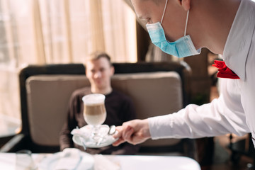 Obraz na płótnie Canvas A European-looking waiter in a medical mask serves Latte coffee.