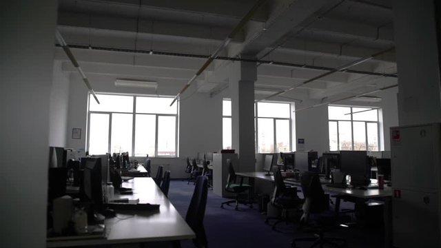 Pan shot of empty open space office with modern and comfortable workplaces. There are desks with laptop, tablet, computers and stationery on them
