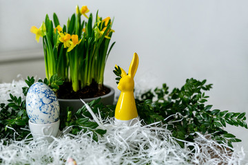 Egg and daffodils. Easter egg decoration, next to yellow porcelain rabbit and yellow narcissi growing in pot, grey background. Easter holiday composition.
