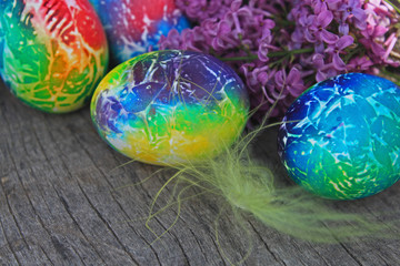 Art decorated eggs with lilac and feather on wooden background.