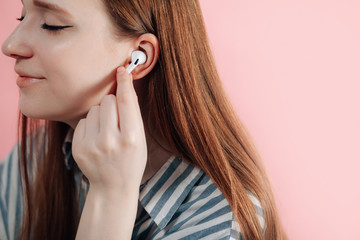 girl uses wireless white headphones on a pink backgroud