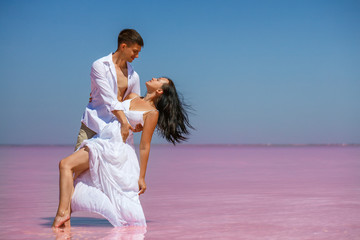 Beautiful young couple in white clothes dancing on a pink lake in the afternoon the sun is shining