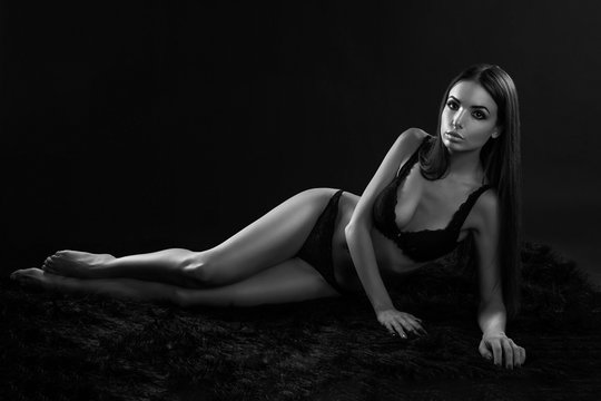 Beautiful young woman lying on a black background in lingerie, black and white photo
