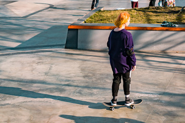 Redhead girl in sweater skateboarding in the skate park. Woman moving fast. Outdoor. Activity in...