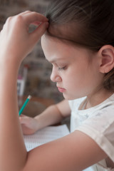 A school-age girl is studying at home at the table. Solves examples in a notebook. Stay at home. Coronovirus.
