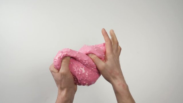 Close-up Top view: pink slime sticks to the hands, then hands stretch the slime. Hands massaging pink slime. White background. Round colored blotches on the slime.