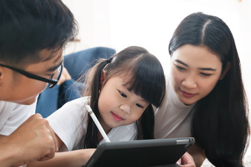Asian family spending time together in living room. Daughter using tablet learning education...