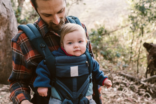 father carrying his baby daughter and taking photos on a hike in the woods