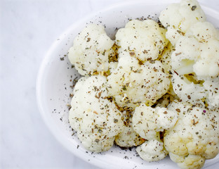 Seasoned roasted cauliflower in white plate on a white marble background.