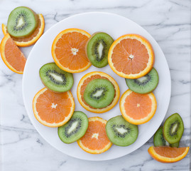 Arrangement of sliced oranges and kiwi on a white plate on a white marble background.