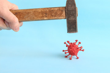 Person holds hummer and hits red model of virus made from plasticine and matches on the blue...