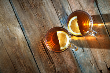 Two cups of tea with lemon on the rustic wooden table. Flare from the light through the cup falls on the table. Cozy morning atmosphere. Top view. Copy space.