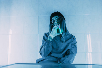 The concept of a COVID-19 scientist wearing safety glasses is experimenting with a vial of antidote that becomes luminescent under UV light in a makeshift laboratory.