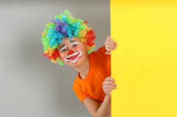 Preteen boy with clown wig looking out of yellow banner on light grey background, space for text....