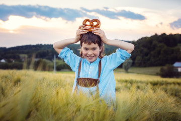 Young Bavarian boy with pretzel in meadow