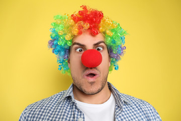 Funny man with clown nose and rainbow wig on yellow background. April fool's day