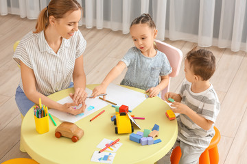 Fototapeta premium Nanny with cute little children playing and drawing at home