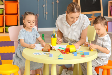 Nanny with cute little children playing and drawing at home