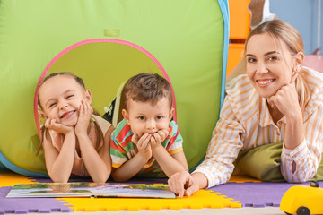 Nanny and cute little children reading book at home