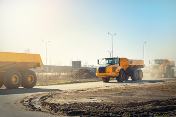 Many big articulated heavy industrial yellow dumper trucks driving on new highway road construction...