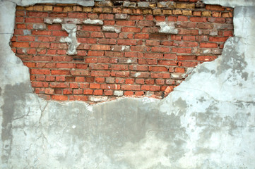 Gray wall with half-peeled plaster, from under which uneven brickwork