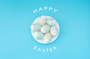 Decorated Easter eggs lie on the white plate on blue background with text. Happy Easter holiday...