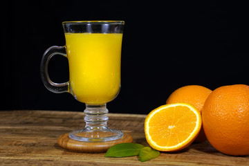 still life with a glass of orange juice, oranges, leaves on a dark wooden background