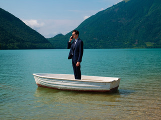 Fototapeta na wymiar Man in suit on a small boat, uses the smartphone to call