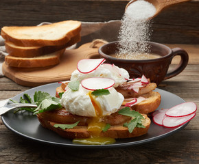 two sandwiches on a toasted white slice of bread with poached eggs, green leaves of arugula and radish in a round plate