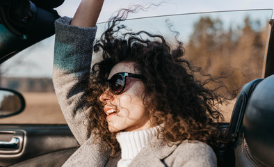 Curly beautiful woman in a convertible car on a sunny day in sunglasses relaxes and feels freedom...