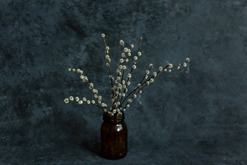 A bunch of fluffy willow twigs in a dark glass vase on a background of burlap.