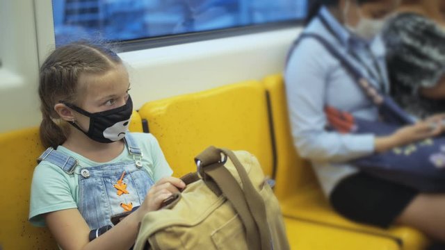 Little girl travel caucasian ride at overground train airtrain with wearing protective medical red mask. Child baby tourist at airtrain with respirator. Pandemic Coronavirus covid-19. People in mask.