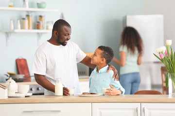 African-American man and his son drinking milk in kitchen