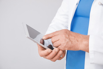 Male doctor with tablet computer on grey background, closeup