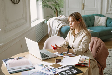 Fashion designer stylist working on new project in the studio, using laptop, magazines,...