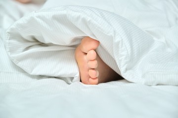 Bare foot of young woman sleeping in white bed, healthy sleep
