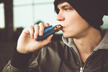 A young man in a black leather jacket smokes a vape.