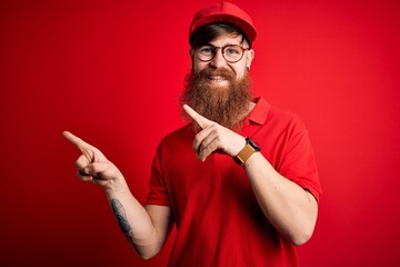 Young handsome delivery man wearing glasses and red cap over isolated background smiling and looking at the camera pointing with two hands and fingers to the side.