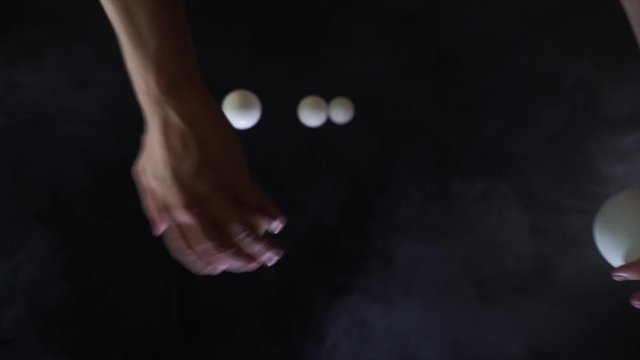 Circus artist wearing black juggling with white balls in slow motion