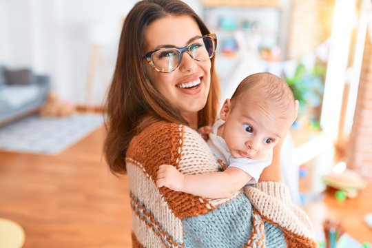 Young beautiful woman and her baby standing at home. Mother holding and hugging newborn