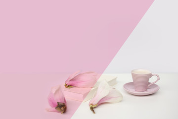 Fototapeta na wymiar cup of cappuccino on a white table, blooming magnolia buds, a book in a white cover on a delicate pink background, a blank for the designer, an invitation form, a spring mood concept