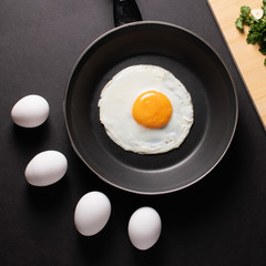 Fried egg in black frying pan with raw white eggs on a black table