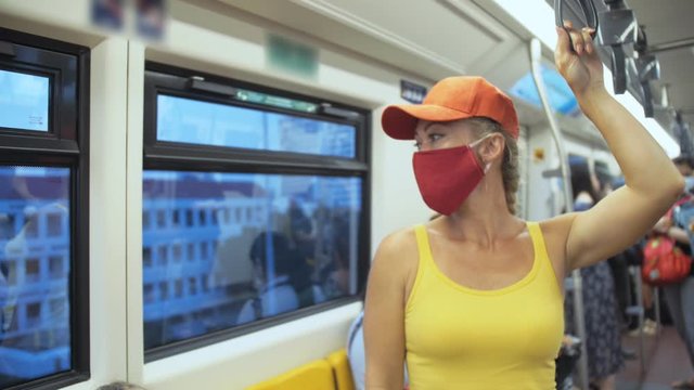 Woman travel caucasian ride at overground train airtrain with wearing protective medical red mask. Girl tourist at airtrain with respirator. Pandemic virus Coronavirus covid-19. People in mask.