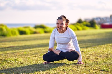 Fototapeta premium Young beautiful sportwoman smiling happy practicing yoga. Coach sitting with smile on face teaching lotus pose at park