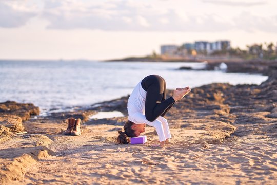 Young beautiful sportwoman practicing yoga. Coach teaching crow pose at the beach