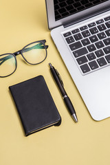 Book, laptop, pen, glasses, yellow background